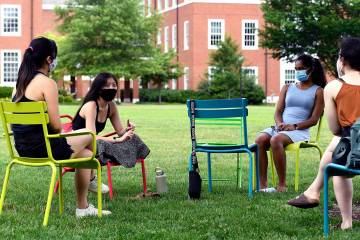 Four socially distanced students sit and talk on a campus quad